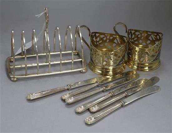 An Edwardian silver toastrack, two gilded white metal cup holders and six silver handles tea knives.